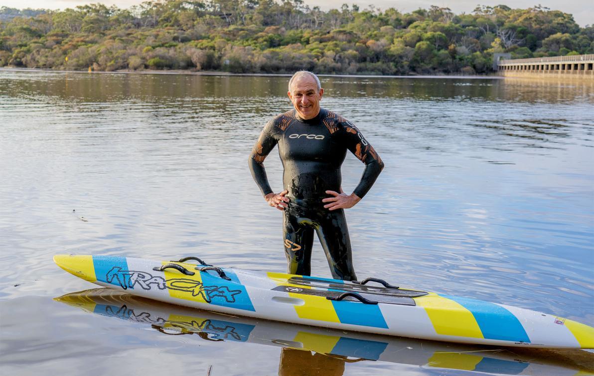 Dementia Advocate Bill in a wetsuit in front of a kayak in shallow water