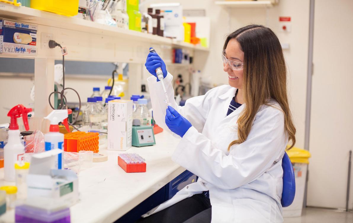 A female researcher sitting in the lab, using a dropper in a beaker