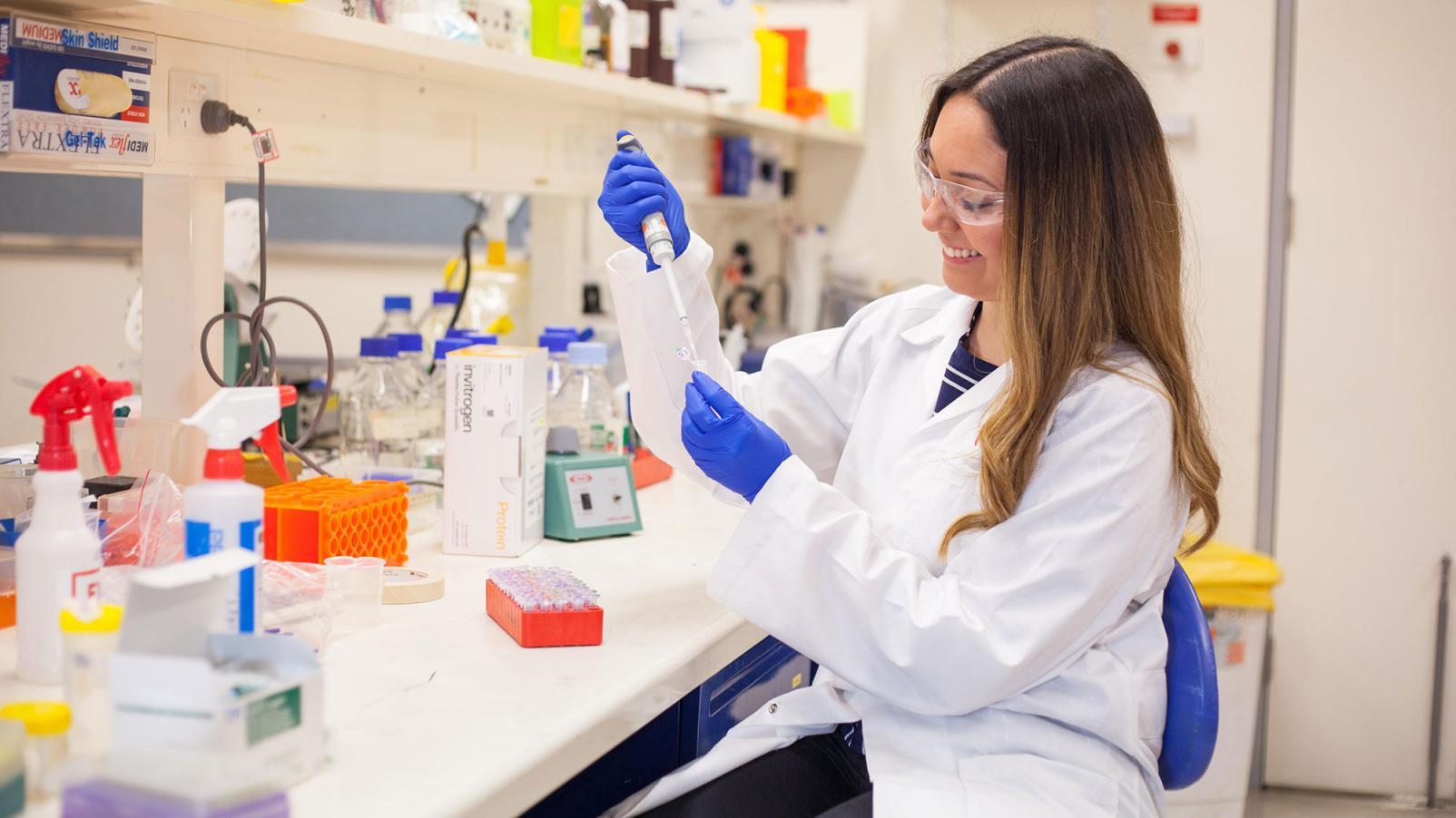A female researcher sitting in the lab, using a dropper in a beaker