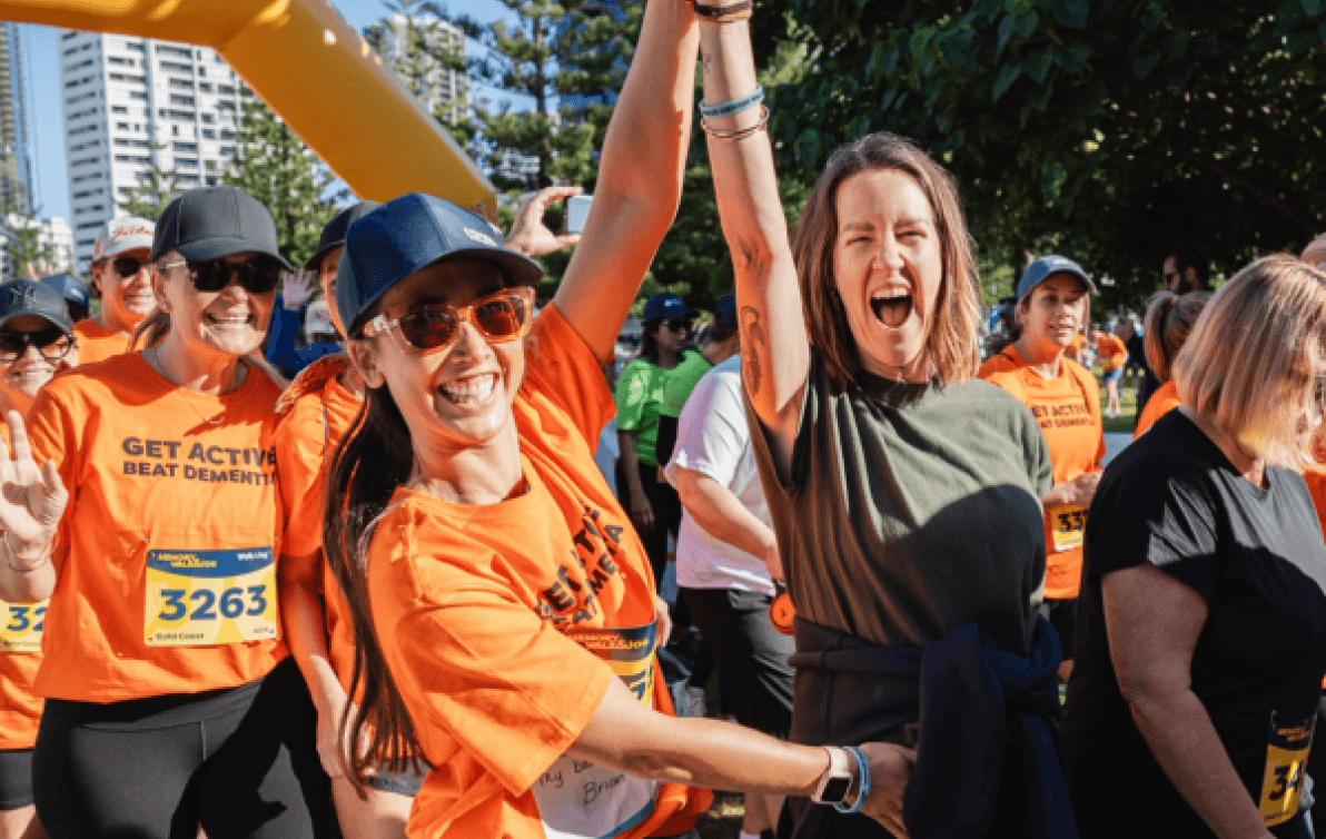 Two women raise their hands triumphantly at the finish line of a Memory Walk & Jog event.