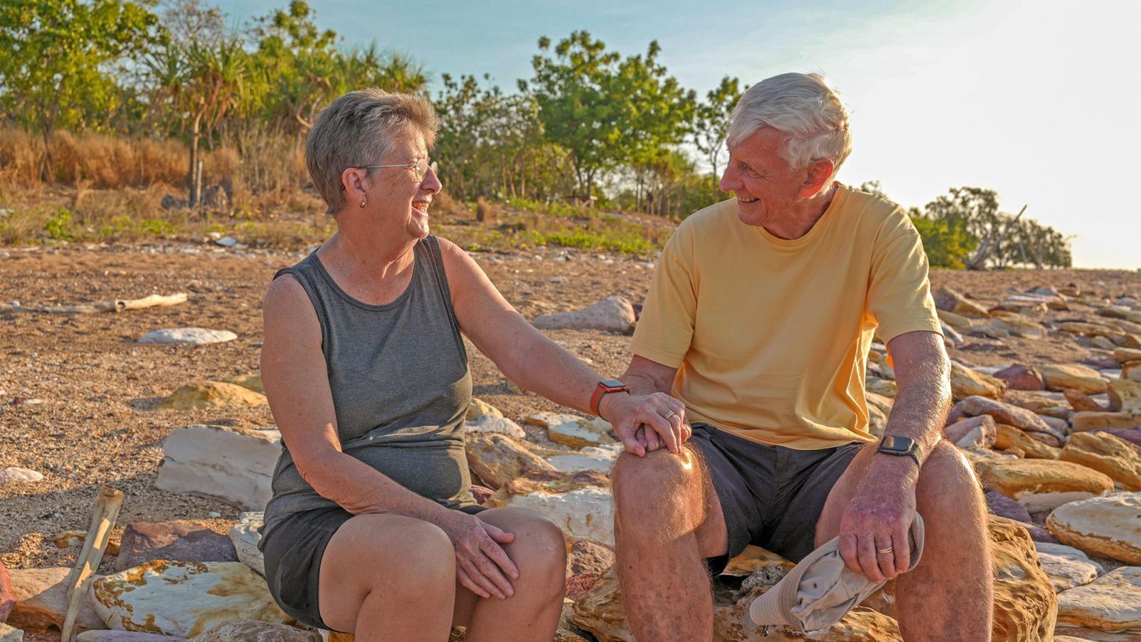 A male and female sitting on a rock in rural Australia smiling at each other