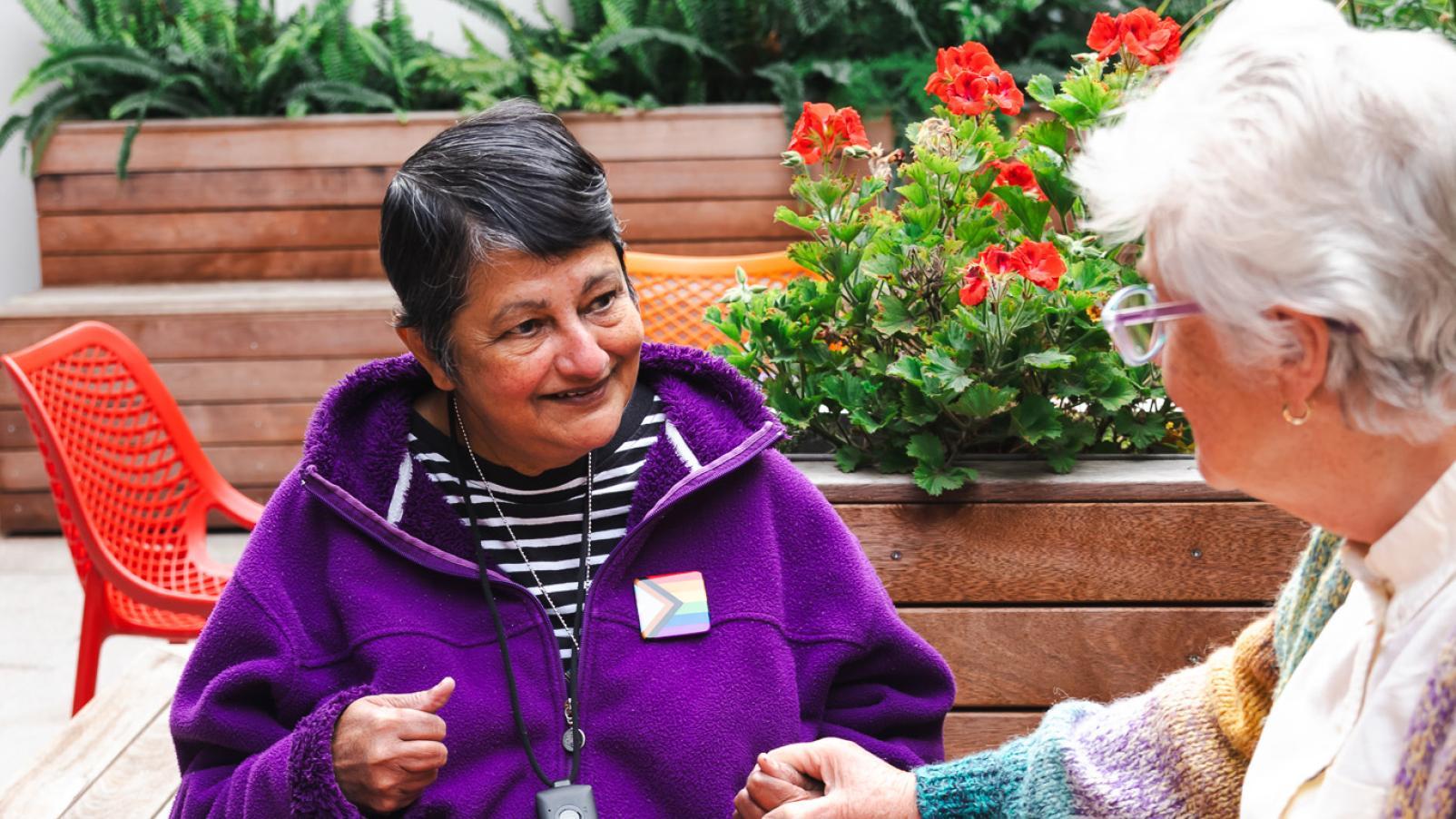 Two women at a café table outside holding hands and smiling.