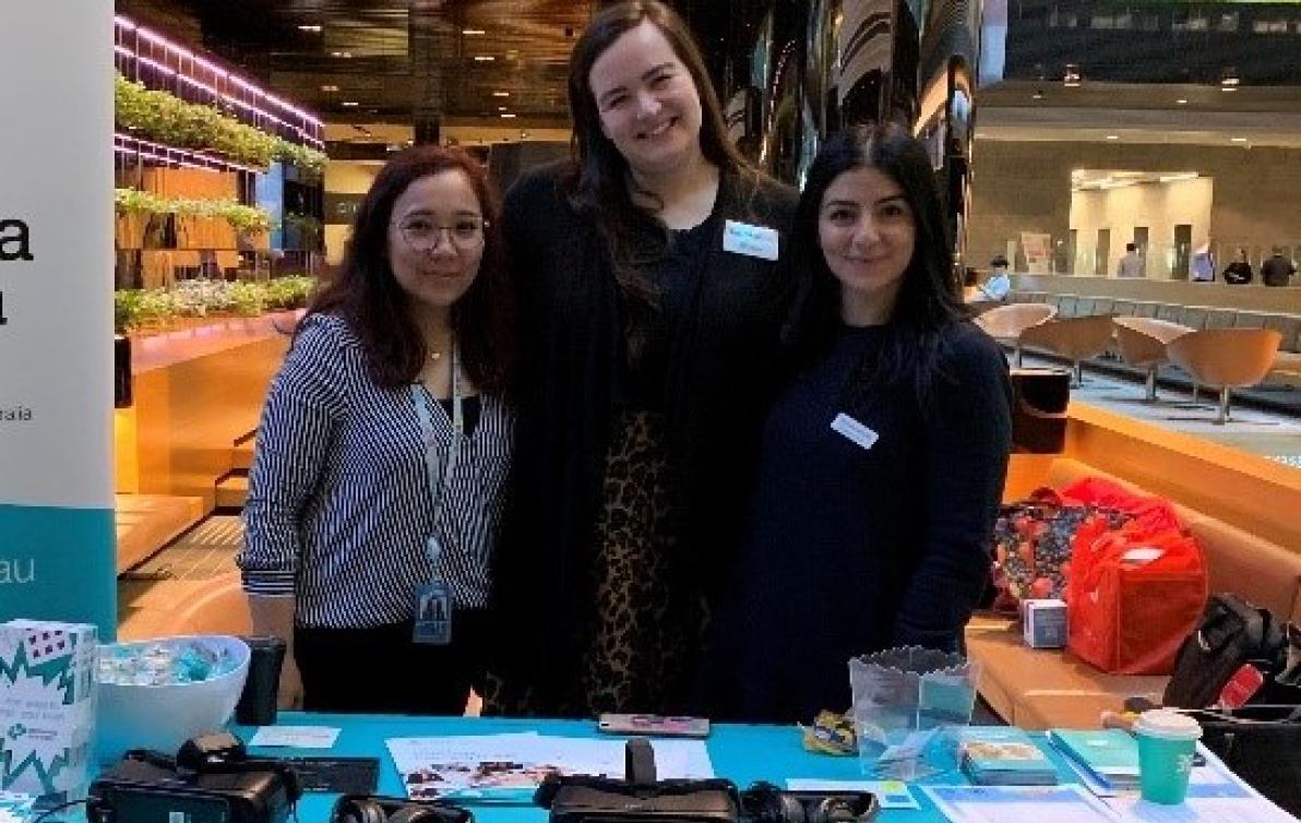 Dementia Australia employees stand in a large hall in front of a table with merchandise on it.